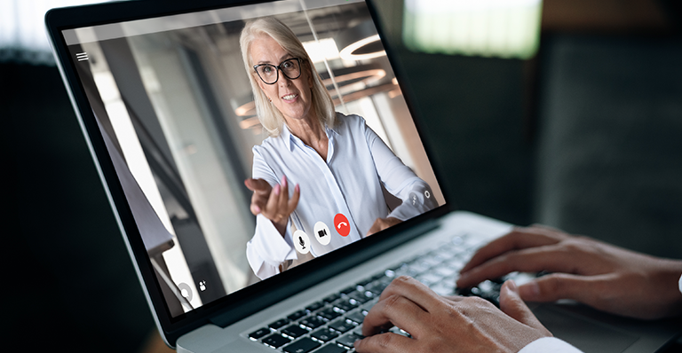 A businessman speaks on a web conference with an advisor using a laptop webcam.