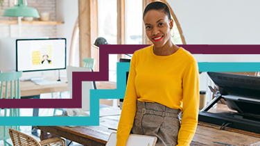 Diverse woman sitting on desk looking directly at camera.