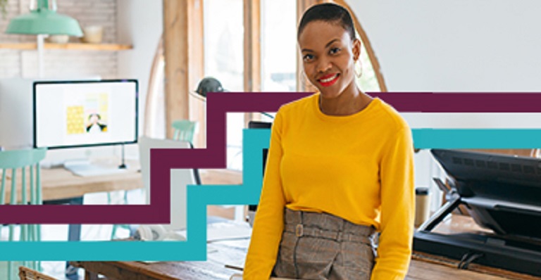 Diverse woman sitting on desk looking directly at camera.