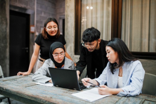 A group of people gathered around a computer to have a discussion