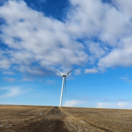 Wind turbine standing in an open field beneath a partly cloudy sky.