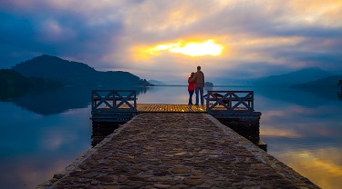 Couple on a dock looking out at the lake during sunset.