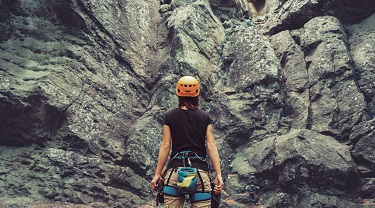 Young woman wearing climbing equipment standing in front of a stone rock outdoors and preparing to climb 