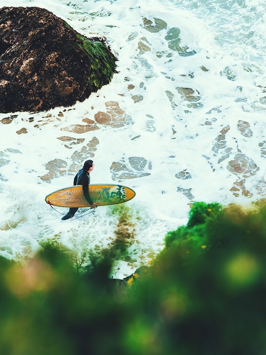 Un surfer transportant sa planche vers des eaux tumultueuses.