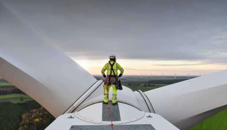 Rope access technician standing on a wind turbine hub at sunrise