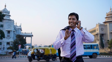 Happy India businessman uses cellphone while walking in busy street