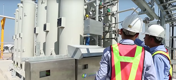 Two men in hard hats standing in front of biomethane tanks.