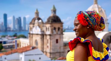 Femme colombienne dans une robe colorée avec des bâtiments en arrière-plan.