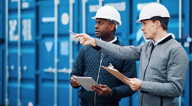 Two businessmen in hard hats with shipping containers in background