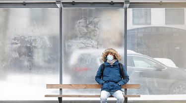 Sick man with a hood sitting alone on bench public transport, wearing protective facial mask