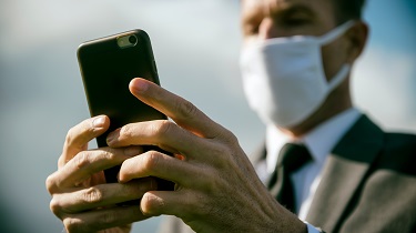 Business man wearing surgical mask sends text on his cellphone