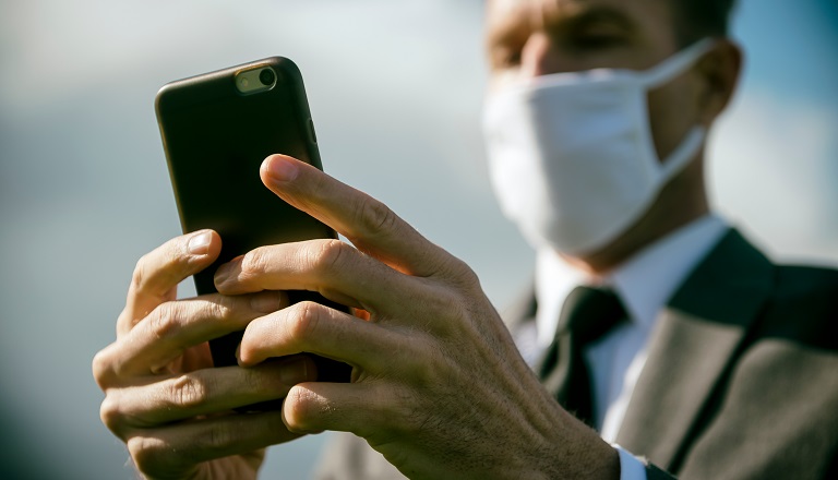 Un homme d’affaires portant un masque chirurgical envoie un message texte avec son téléphone cellulaire.