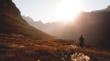 a man is walking in the valley of a mountain facing the sun