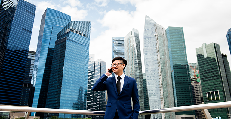 Un homme asiatique souriant se tient devant les gratte-ciel de Bangkok