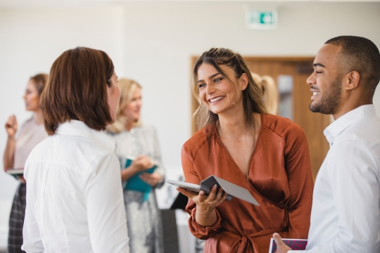 Group of diverse young professionals smiling, listening, and networking at a business conference.