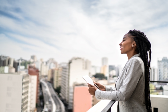 Enthusiastic black female entrepreneur looking out at the city skyline from a rooftop.