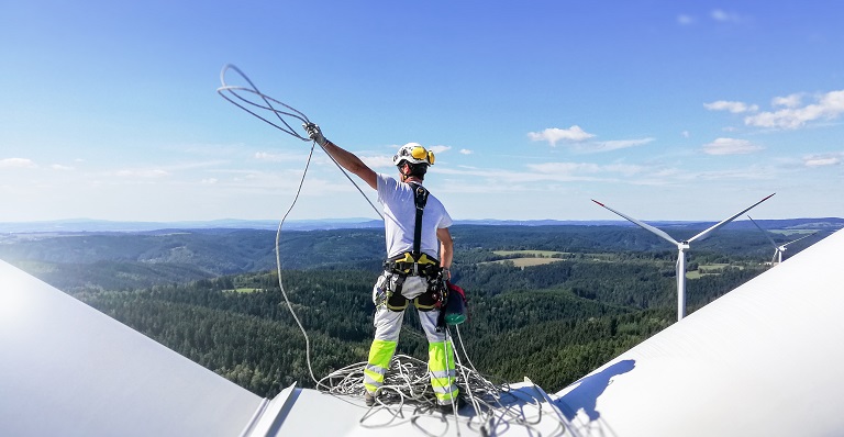 Mechanic wearing safety harness stands atop of wind turbine.