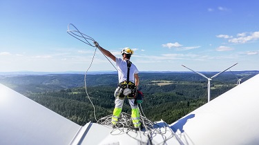 Un mécanicien portant un harnais de sécurité se dresse au sommet de l'éolienne.