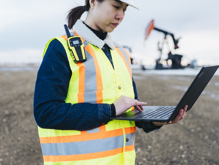 Female oil worker uses laptop in the field.