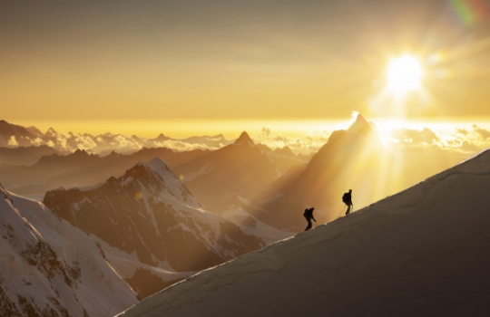 Climbers on a snowy ridge at sunrise.