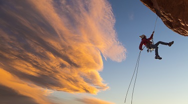 Female climber rappelling down a sheer cliff