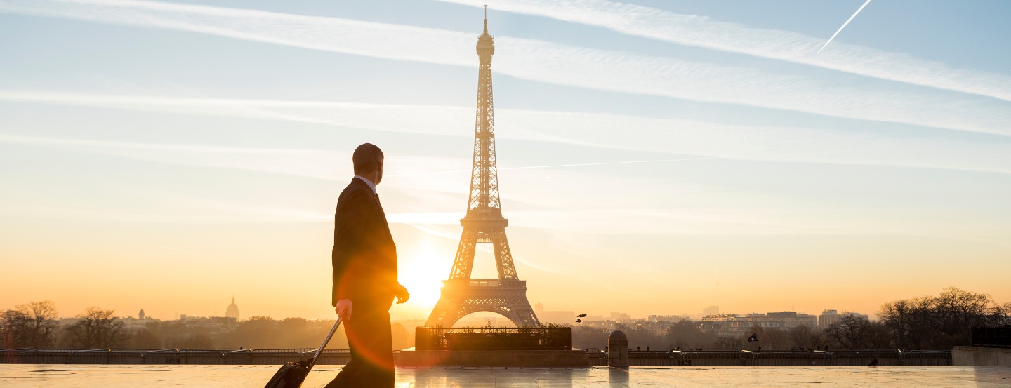 Magnifique lever de soleil sur Paris avec la tour Eiffel en arrière-plan, tandis qu’un homme d’affaires marche avec ses bagages.