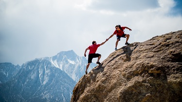 Un alpiniste aide un autre alpiniste à se hisser au sommet d’un immense rocher.