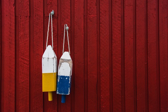 two wooden buoys against a red fence