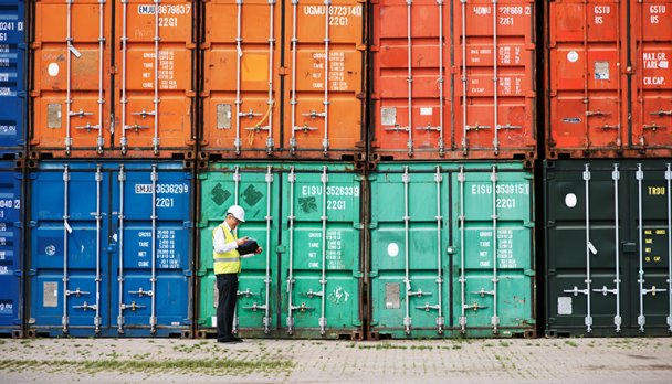 An inspector standing in front of large, colourful shipping containers