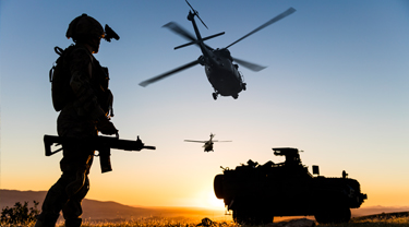 un militaire se tient au coucher du soleil avec un hélicoptère survolant