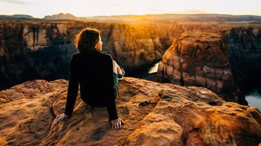 A person sitting on a rock in a mountainous landscape.