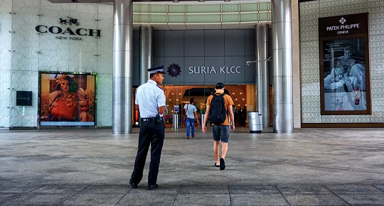 A man enters an upscale shopping plaza while a policy officer looks on.