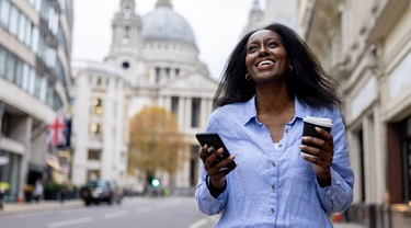 Smiling business woman checking her cellphone on urban street in Britain