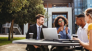 Installée à une table à l’extérieur, une dirigeante explique la nouvelle stratégie d’affaires à son équipe.