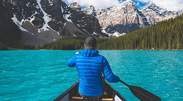 A canoeist paddles across a blue lake.