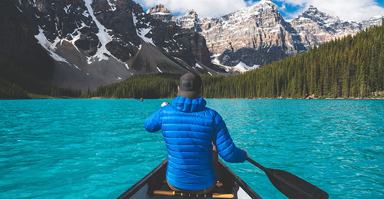 A canoeist paddles across a blue lake.