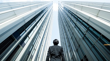 Businessman surrounded by tall steel buildings looks to the sky