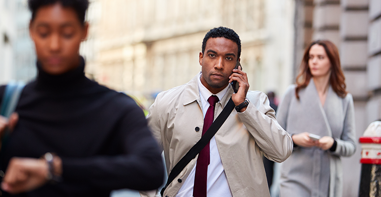 Black executive walks in busy London street using phone.