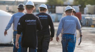 Five men wearing construction hats and CarboNet shirts walking outdoors, facing away from the camera.