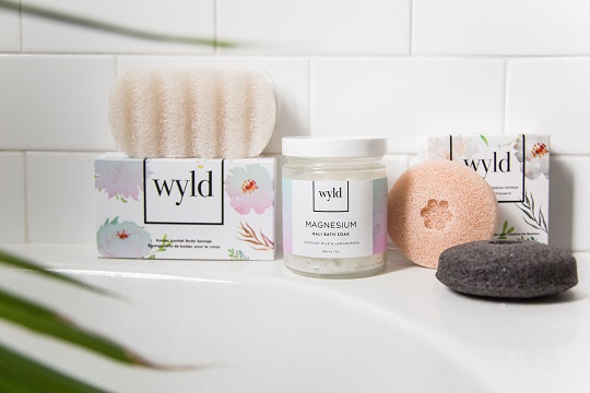 Des éponges et des sels de bain de Wyld Skincare sur le rebord d’une baignoire