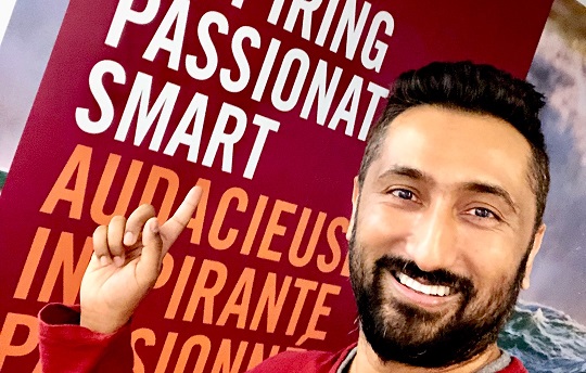 A smiling EDC employee points to a banner with the words daring, inspiring, passionate and smart