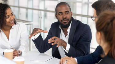 Man in blue blazer talking to group around a table