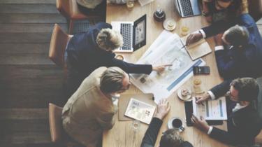 A group of business people sitting at a conference table as seen from above.