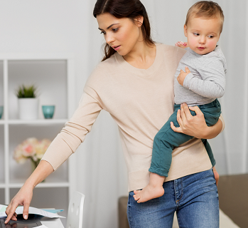 Mother holding child while working on a laptop