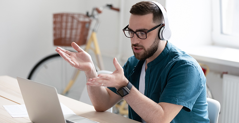 A man wearing headphone is talking during a conference call on his computer.