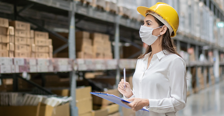 An employee wearing a hardhat is verifying inventory of a warehouse.