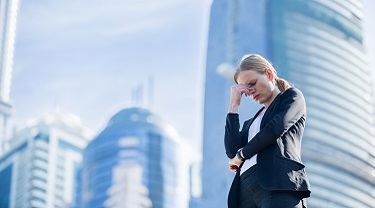 Une femme d’affaires paraît troublée et supporte sa tête d’une main à l’extérieur de son lieu de travail.