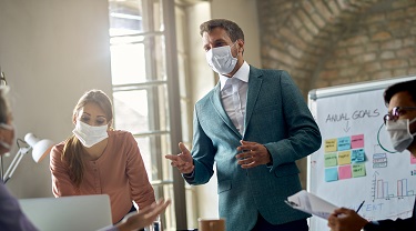 Male employer wearing a face mask explains corporate goals to his staff.