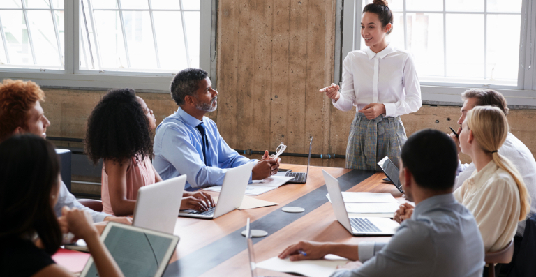 Femme faisant une présentation à un groupe réuni autour d’une table de conseil