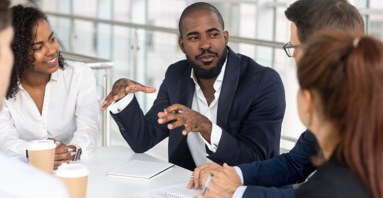 Man in blue blazer talking to group around a table